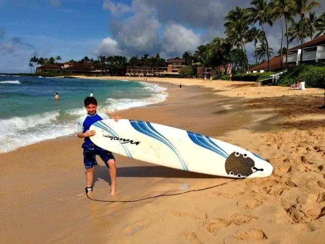 boy holding large surfboard on beach in kauai