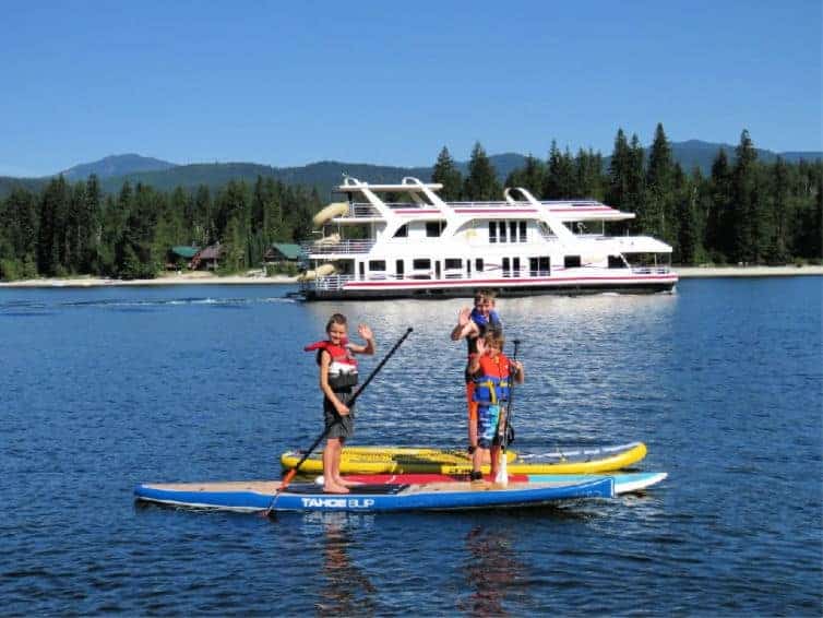 kids on sup boards waving in front of houseboat