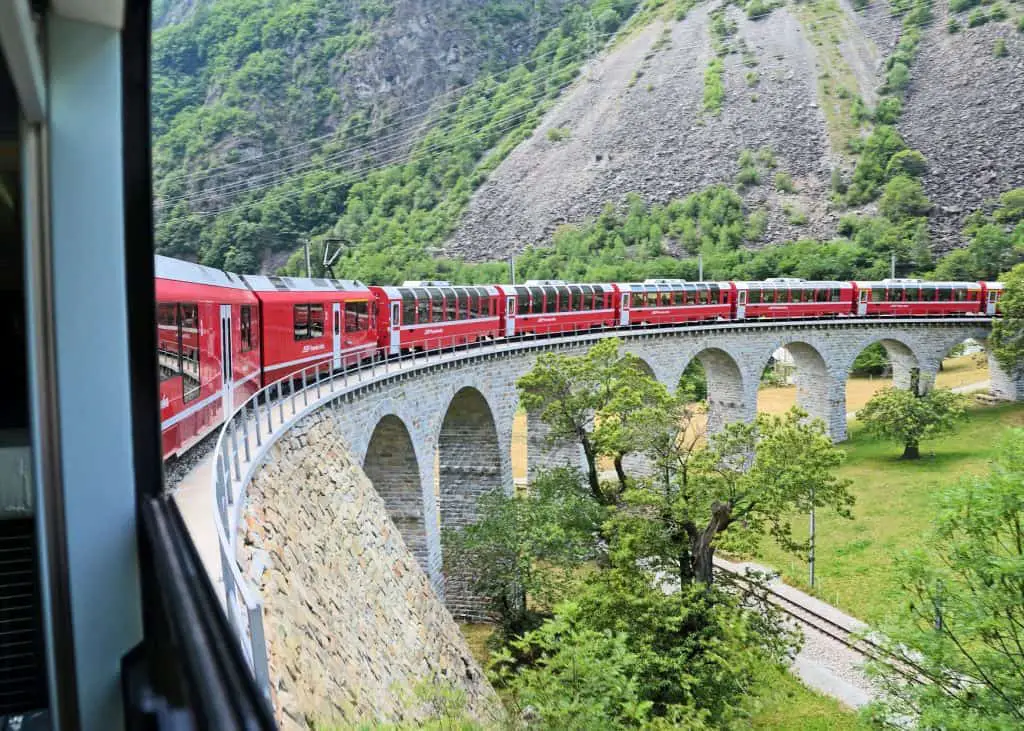 red swiss train over stone bridge