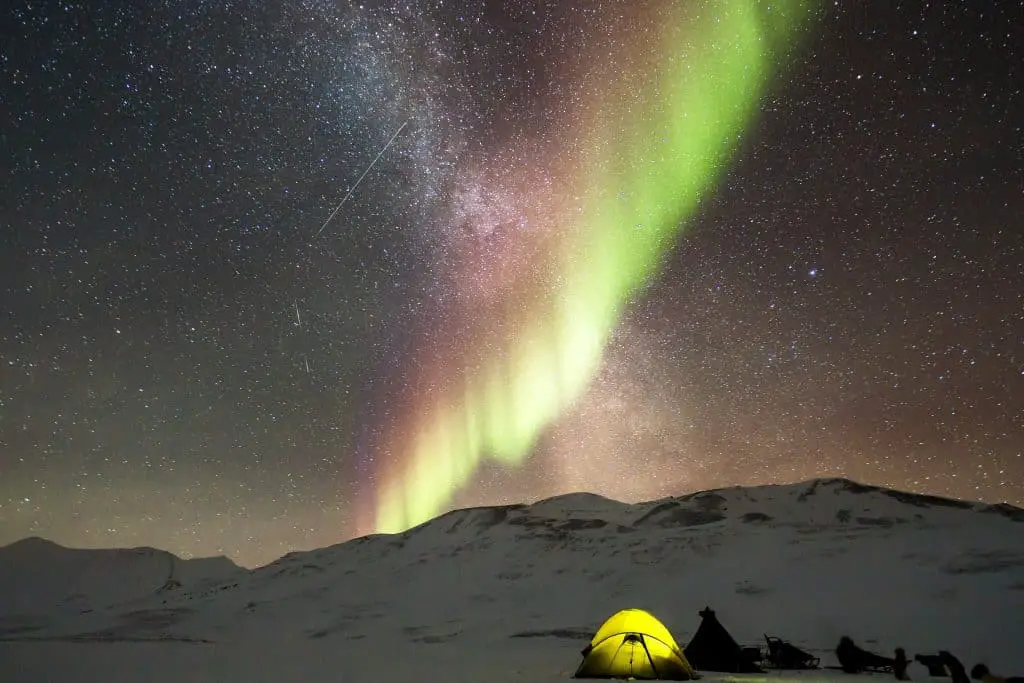 yellow tent in snow with northern lights