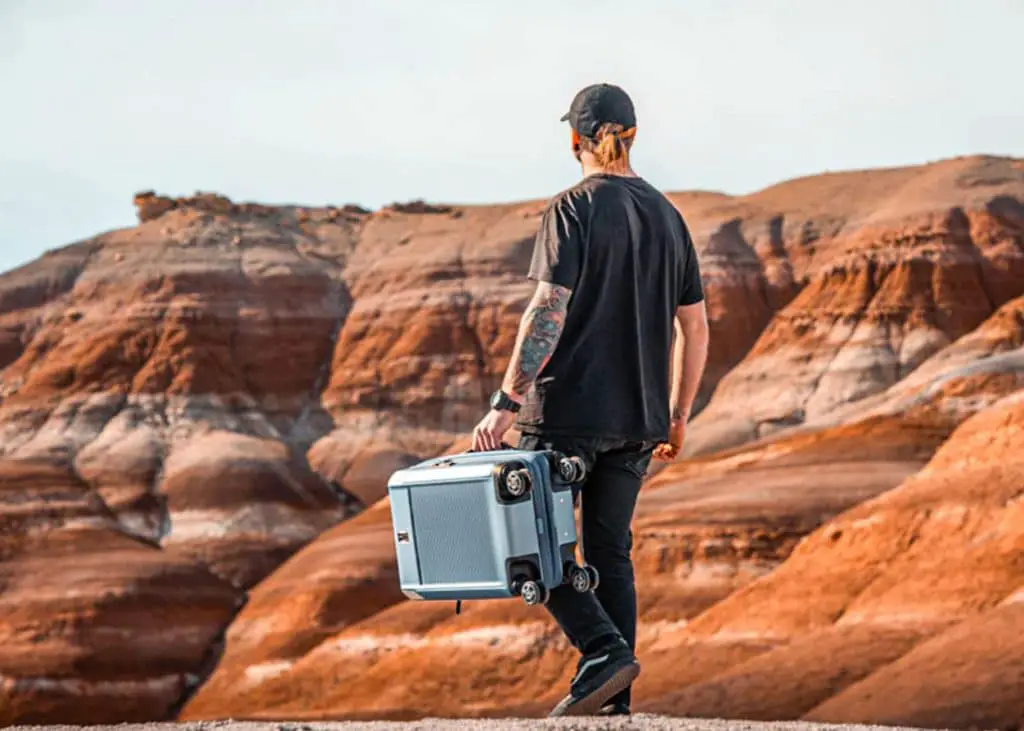 man holding blue travelpro suitcase in desert